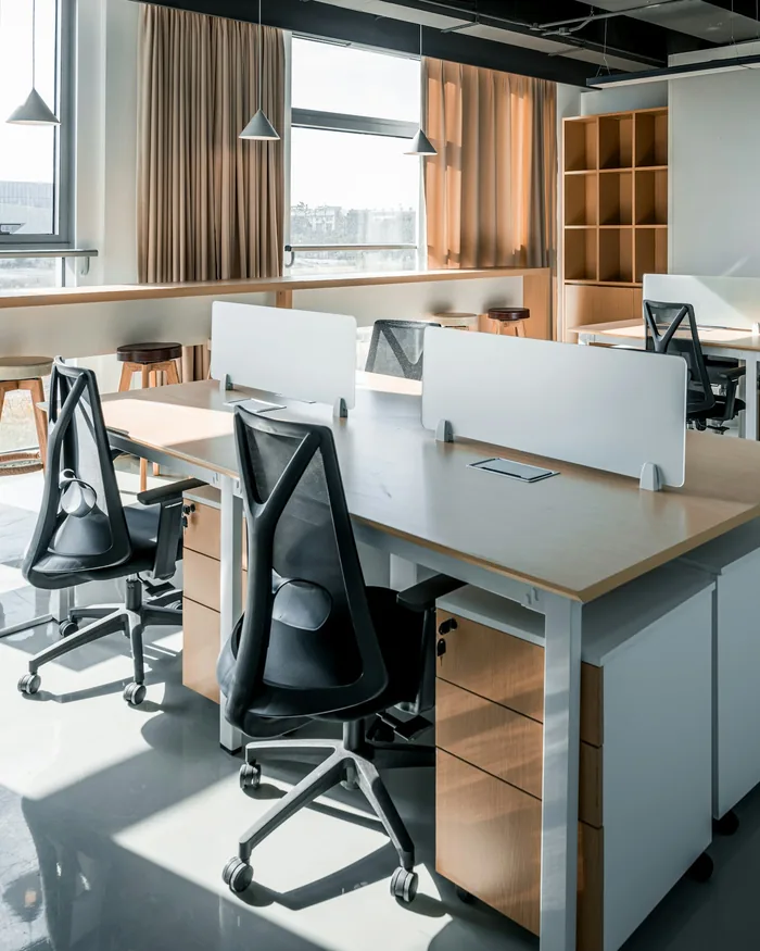 Oficina diáfana y ordenada, con mesas de madera y luz natural
